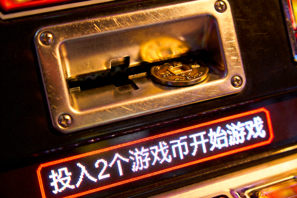 游戏机台上的投币口特写，显示需要投入2个游戏币才能开始游戏